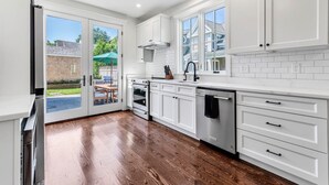 A modern kitchen with white cabinetry, a stainless steel dishwasher, and a large window overlooking a backyard.