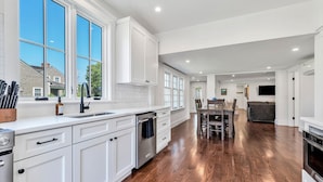 A spacious kitchen with white cabinetry, a large window, and a dining area with a wooden table and chairs.