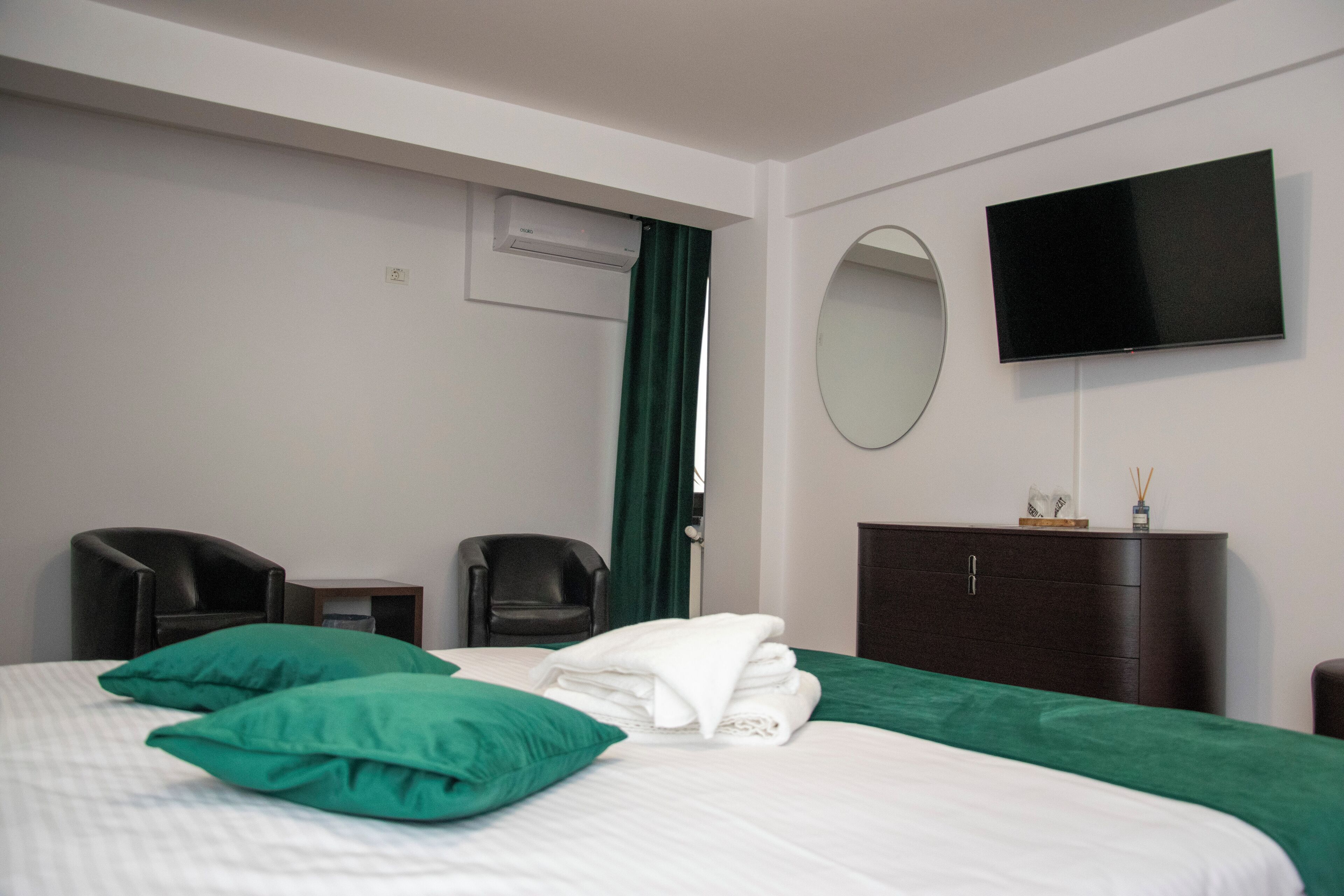 Une chambre d’hôtel avec un lit, deux chaises, une télévision, un miroir et une commode.