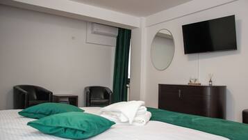 Une chambre d’hôtel avec un lit, deux chaises, une télévision, un miroir et une commode.