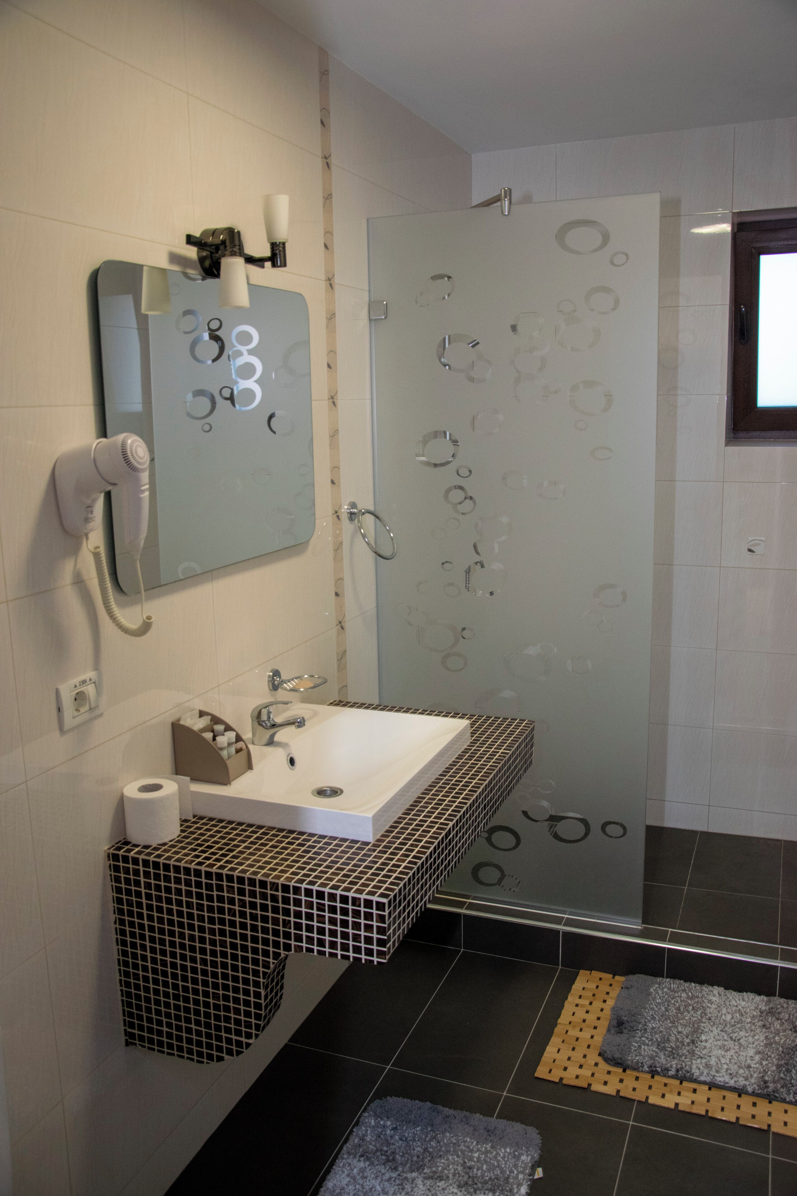 A modern bathroom with a white sink, a mirror, and a hairdryer on the wall.