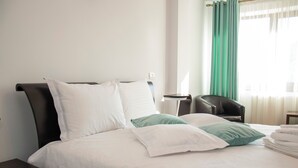 Een net opgemaakt bed met witte en groene kussens, een donker hoofdbord, en een stoel ernaast.