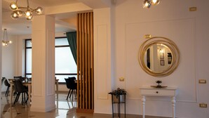 Een hotellobby met een eetgedeelte, een spiegel met gouden lijst en een potplant op een consoletafel.