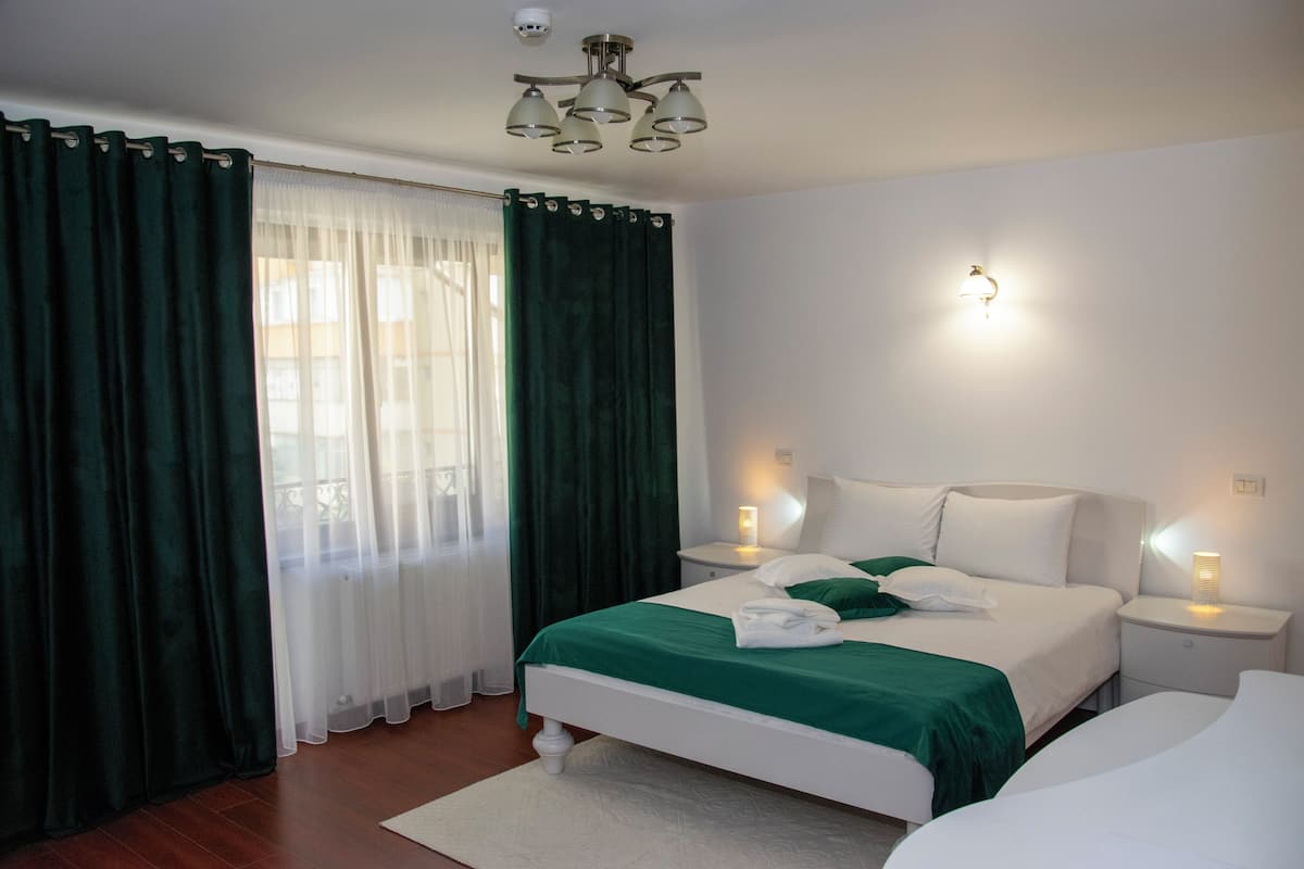 Habitación de hotel con cama, dos mesitas de noche, una lámpara y una ventana con cortinas.