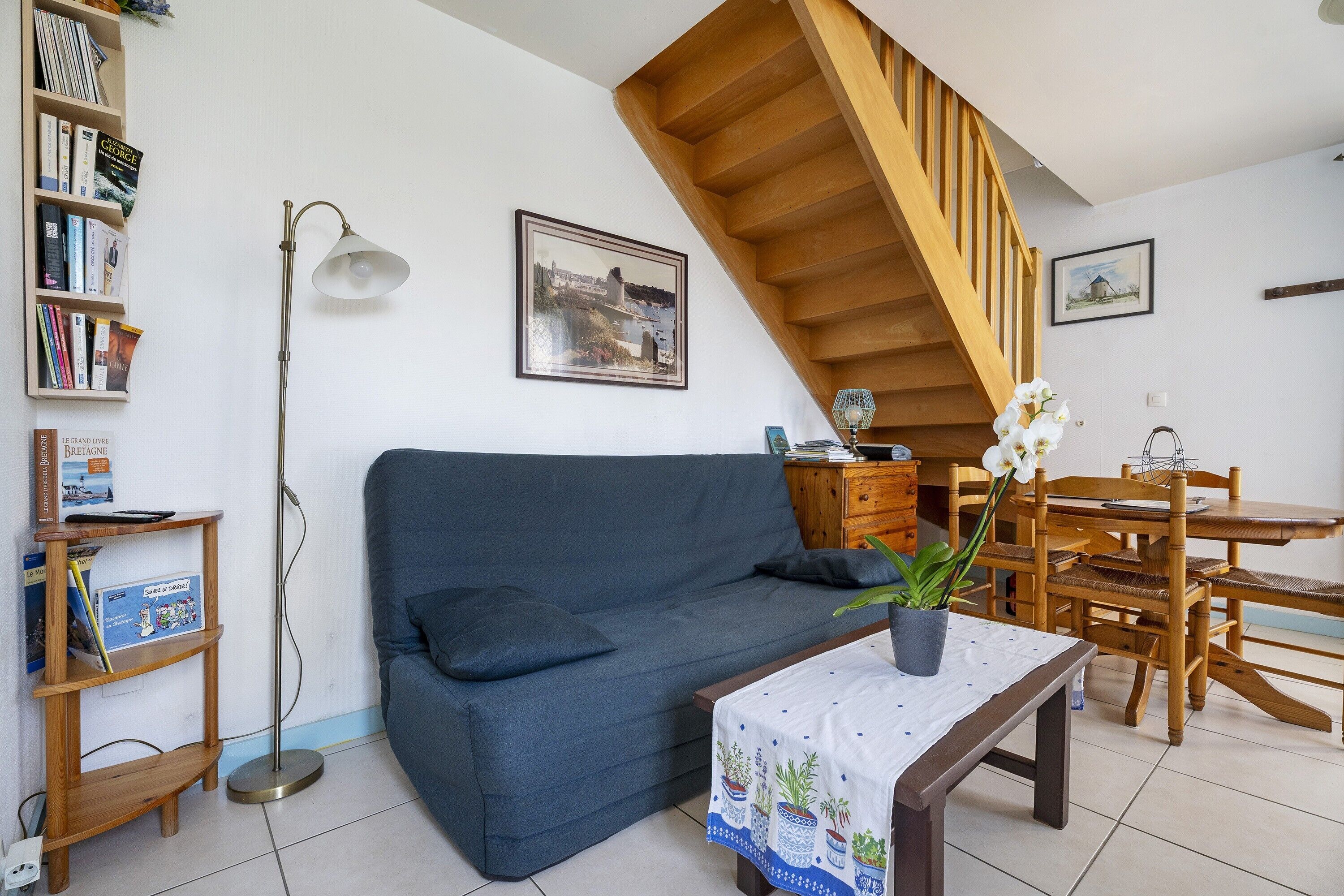 A living room with a sofa, a dining table, a bookshelf, and a staircase.