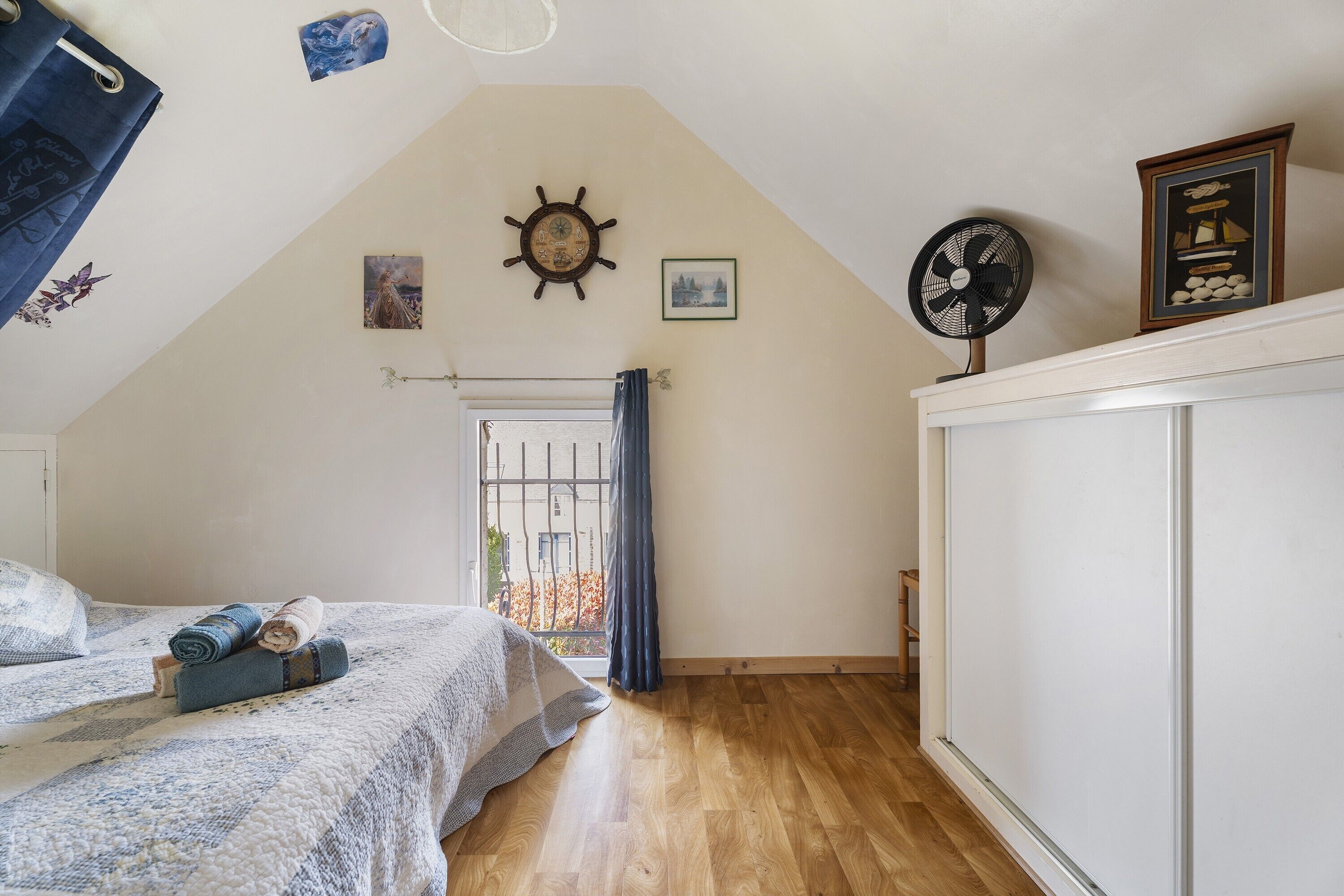 Een slaapkamer met een bed, een ventilator, een klok en een raam met gordijnen.