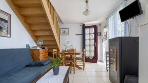 Ein Wohnzimmer mit einer Couch, einem Esstisch, Stühlen, einer Treppe, einem Fernseher und einem Kühlschrank.