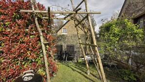 Ein Garten mit einem hölzernen Spalier, einem Grill und einem Haus im Hintergrund.