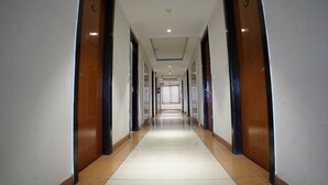 Un long couloir étroit, avec des portes en bois de chaque côté et un sol carrelé.