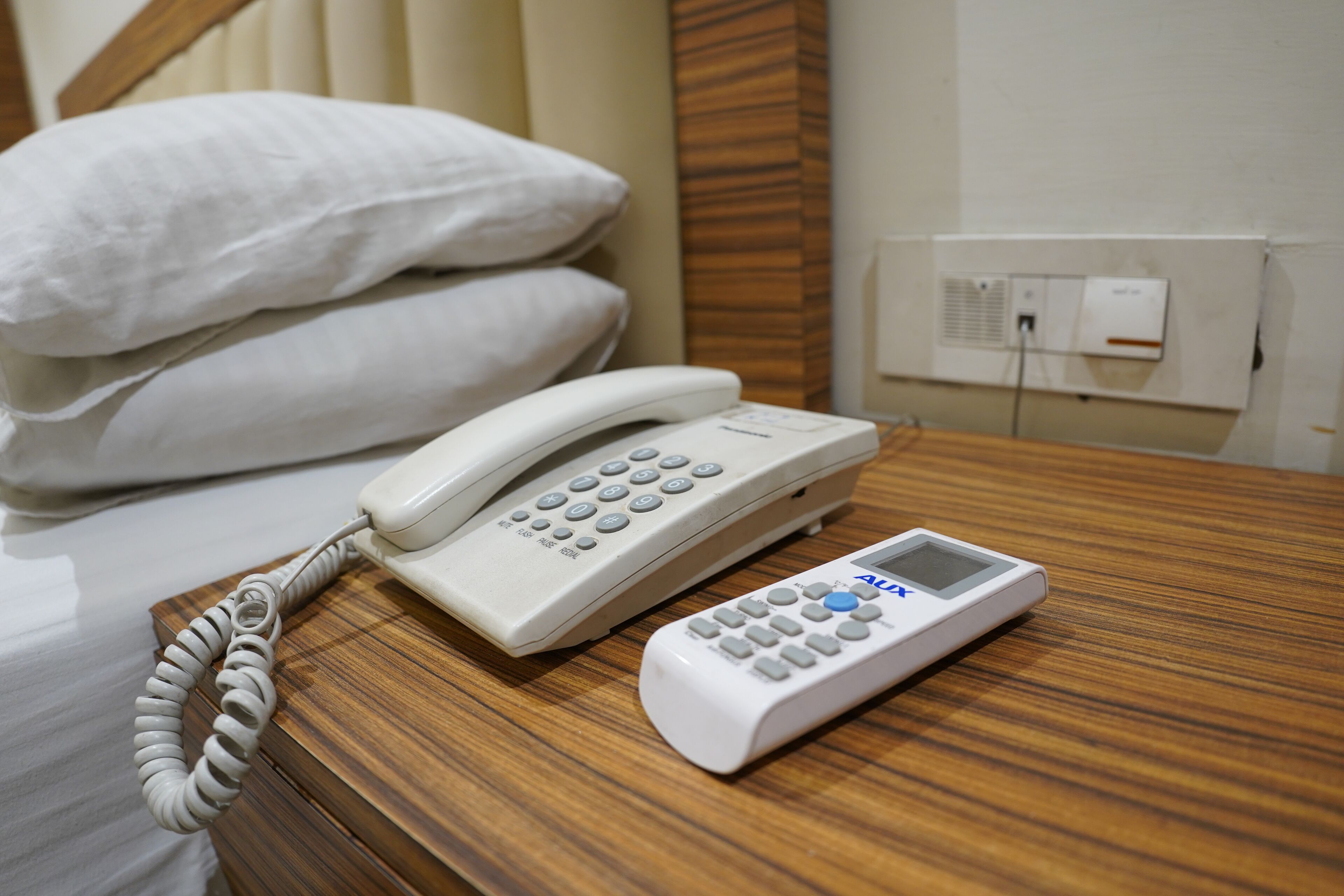 Ein Hotelzimmer mit Nachttisch aus Holz, einem weißen Nachttischtelefon und einem digitalen Wecker.
