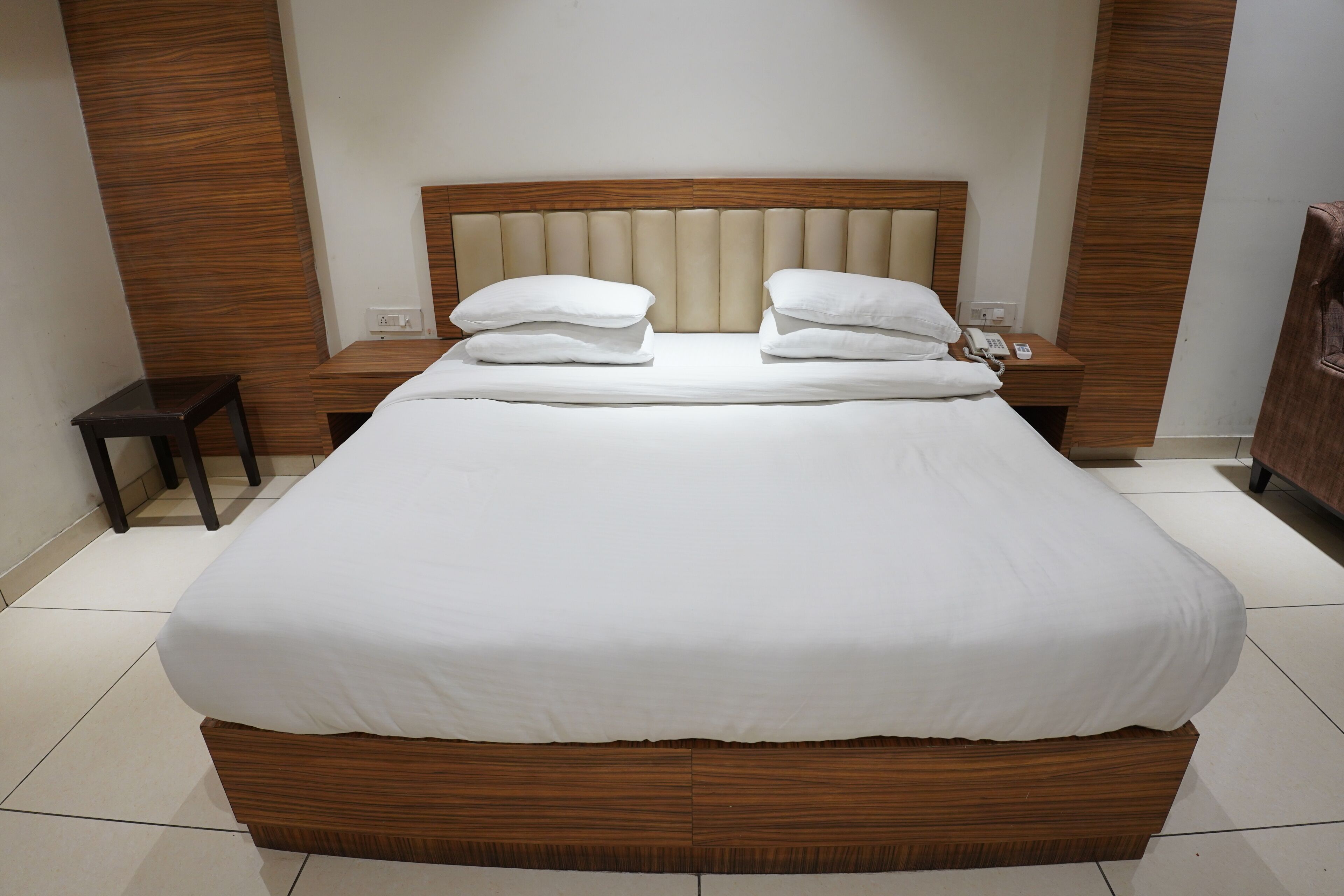 A neatly made bed with a wooden headboard and two pillows, a bedside table with a lamp, and a small nightstand.