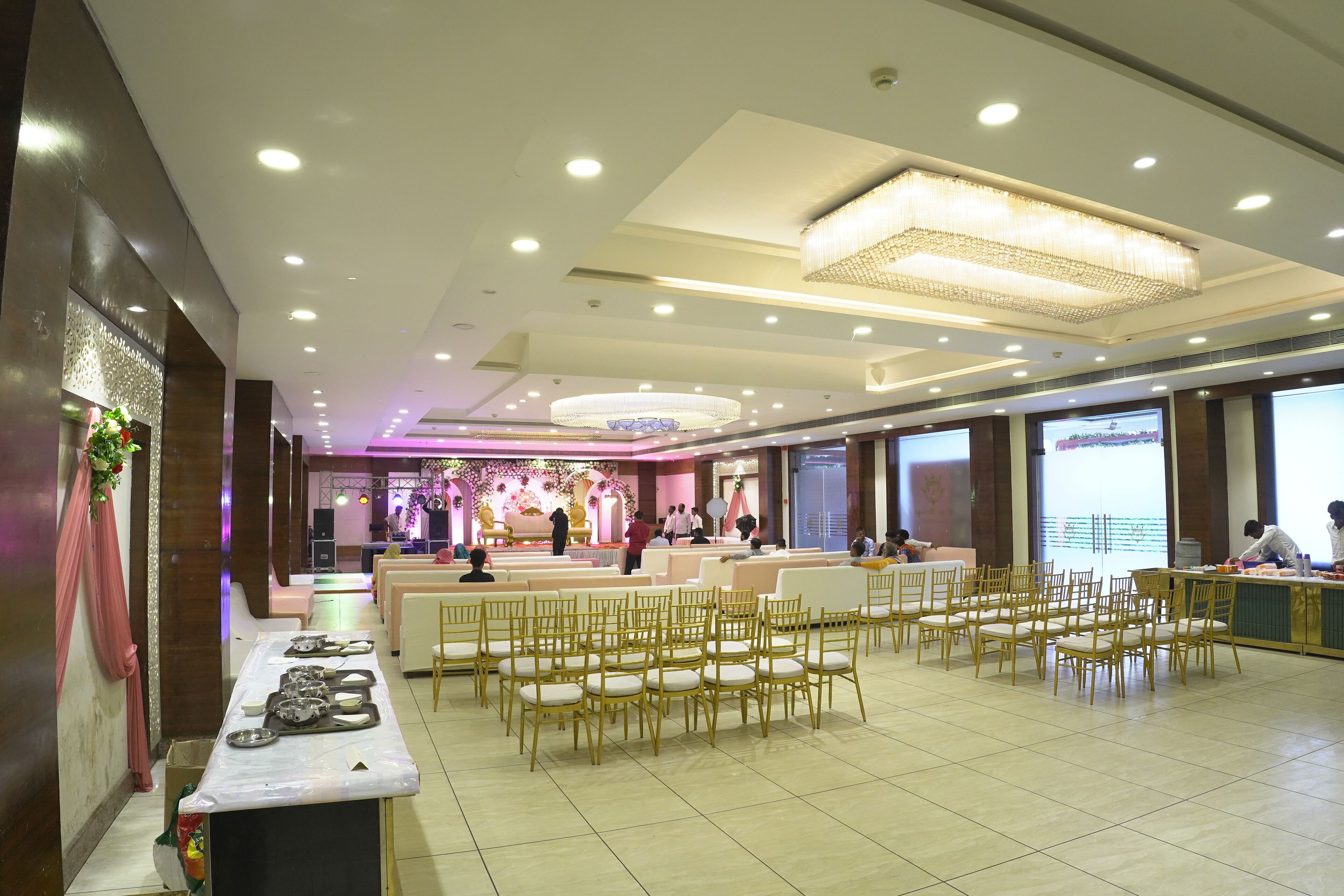 A spacious hall with rows of chairs, a stage with a floral backdrop, and a reception area with a counter.