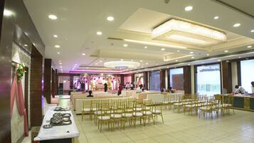 A spacious hall with rows of chairs, a stage with a floral backdrop, and a reception area with a counter.