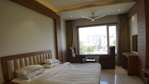 Une chambre d’hôtel avec un grand lit, un bureau, une chaise et une vue sur la ville par la fenêtre.