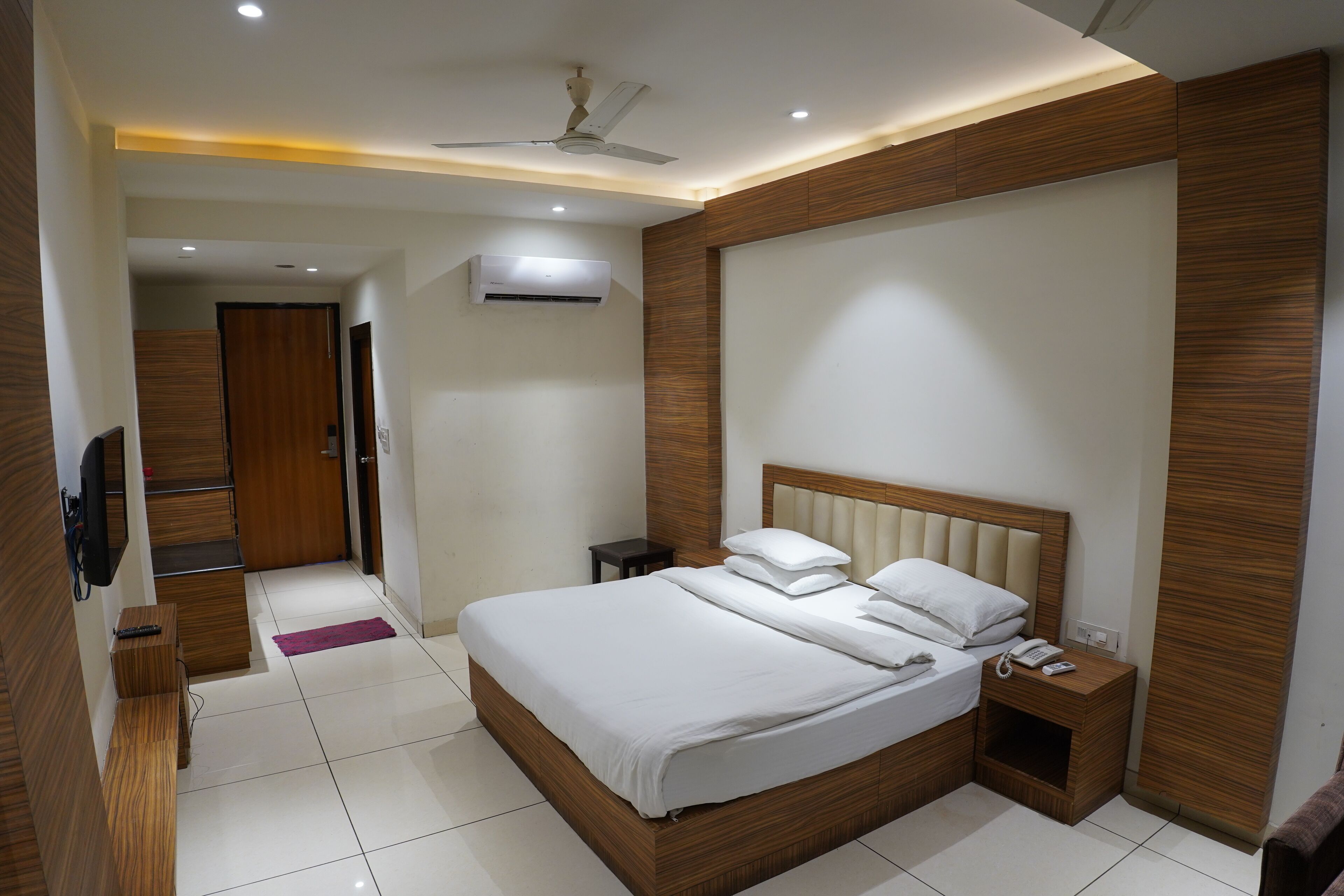 A modern hotel room with a large bed, bedside tables, a ceiling fan, and an air conditioning unit.