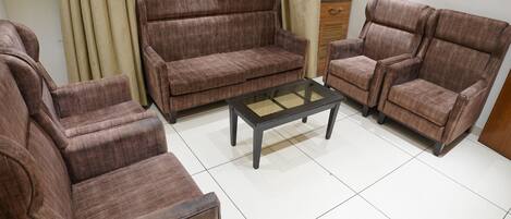 Una sala de estar con un sofá marrón, una mesa de centro de vidrio y un mueble de madera.