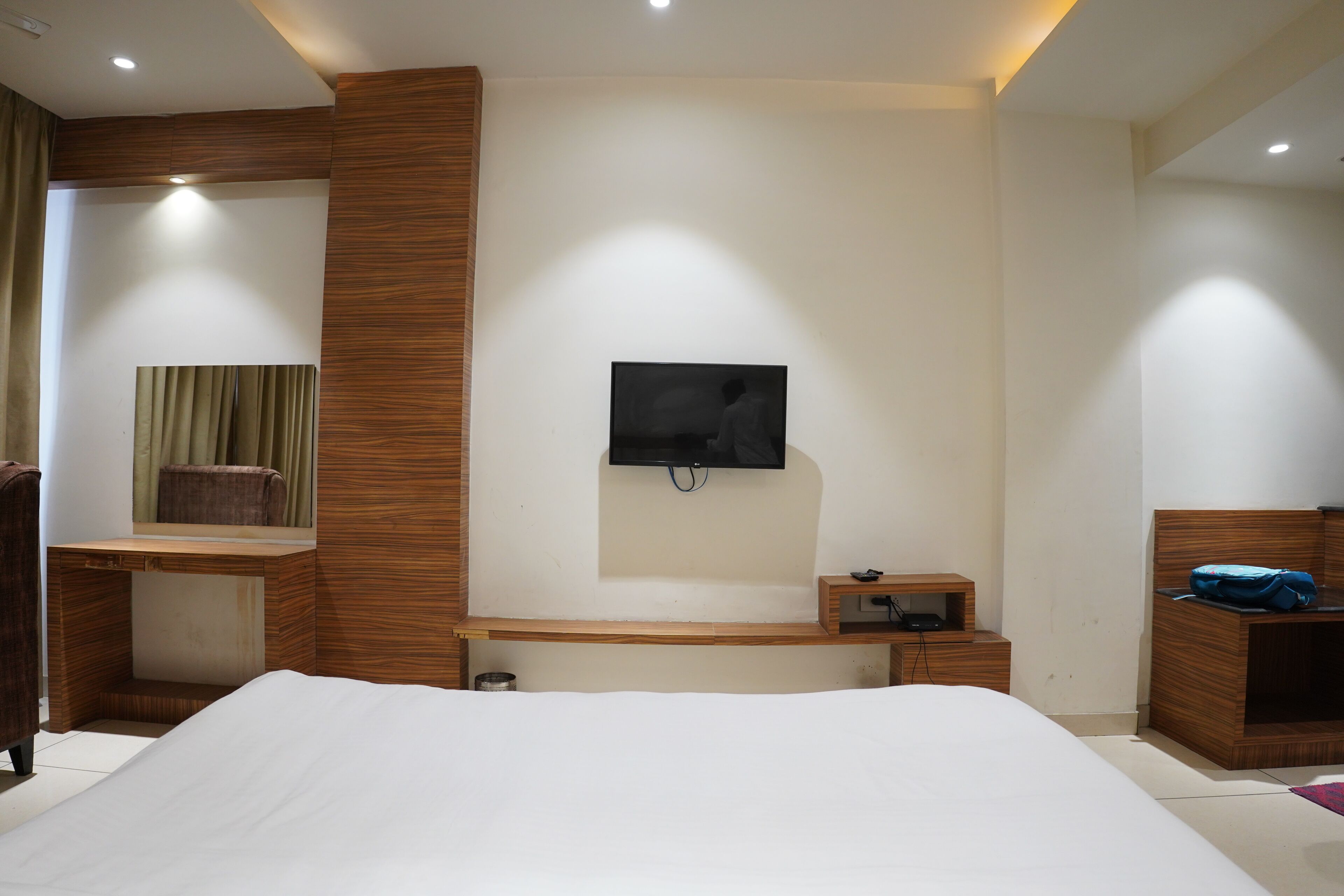 Una camera da letto moderna con un letto grande, una scrivania in legno, una TV fissata al muro e un comodino.