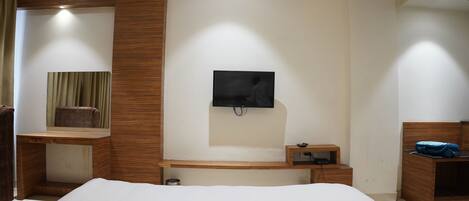 Un dormitorio moderno con una cama grande, un escritorio de madera, un televisor montado en la pared y una mesita de noche pequeña.