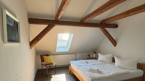 A bedroom with a sloped ceiling, wooden beams, a skylight, a bed, a chair, and a radiator. - Country house by the lake with fenced plot in Brandenburg an der Havel (Brandenburg)