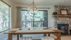 A dining area with a wooden table and benches, a stone fireplace, and a view of trees through large windows. - Summit #27: 1  BR, 1  BA Condominium in Mammoth Lakes, Sleeps 4 (Mammoth Lakes)