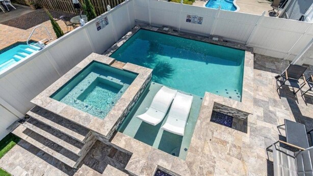Una piscina rettangolare con una vasca idromassaggio e due lettini.