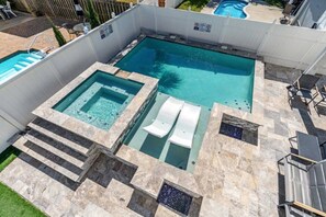 Una piscina rectangular con un jacuzzi y dos sillas de descanso.