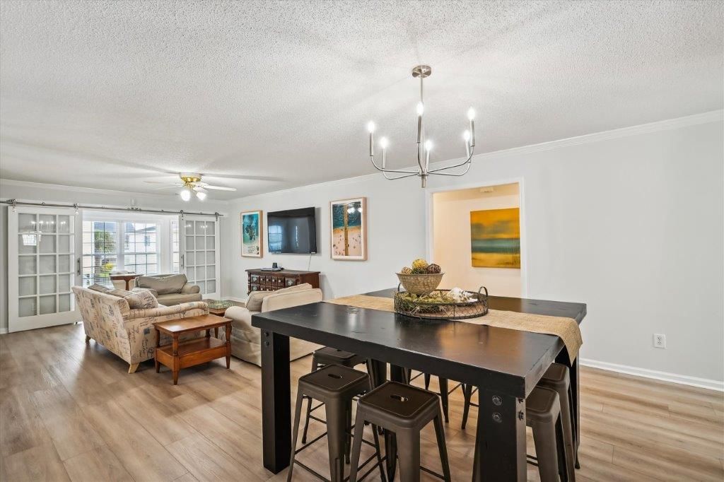 A spacious living room with a dining area, large windows, and a chandelier.