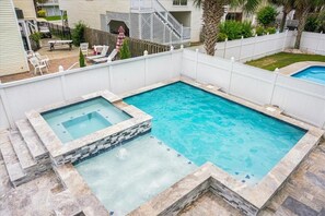 A rectangular swimming pool with a hot tub section, surrounded by a white fence, with a patio area and outdoor furniture visible in the background. - 6br sleeps 24 w/pool & hot tub, golfcart (North Myrtle Beach)
