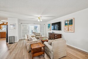 A living room with a sofa set, a coffee table, a TV, and artwork on the wall. - 6br sleeps 24 w/pool & hot tub, golfcart (North Myrtle Beach)