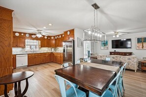 A modern kitchen with wooden cabinets, a stainless steel refrigerator, and a dining area with a table and chairs. - 6br sleeps 24 w/pool & hot tub, golfcart (North Myrtle Beach)