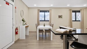 Habitación de hotel moderna con zona de comedor, una puerta blanca con señalización de salida de emergencia, un extintor y una ventana con vistas a árboles cubiertos de nieve.