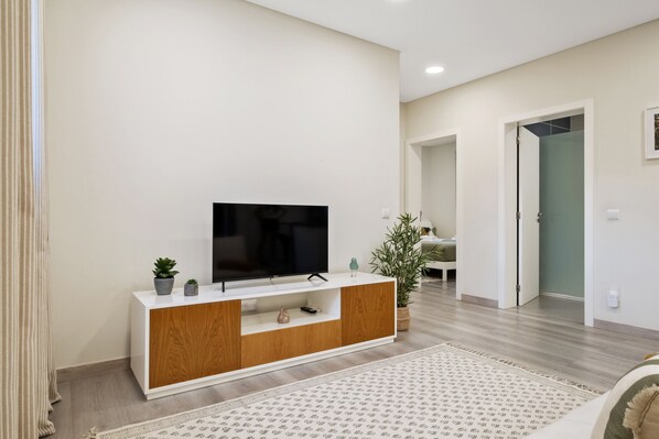 A modern living room with a flat-screen TV on a white and wood console, a patterned rug, and a potted plant.