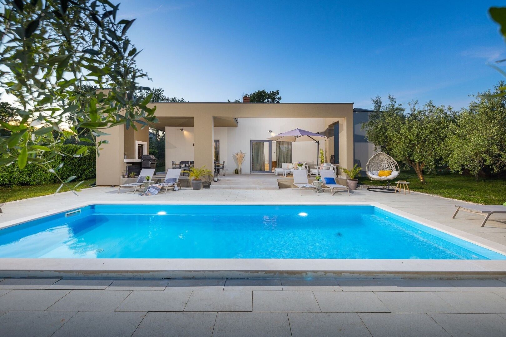 A modern outdoor pool area with lounge chairs and a covered seating area.