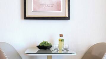 A dining area with two chairs, a table, a framed picture, a bowl of grapes, and a bottle of drink.