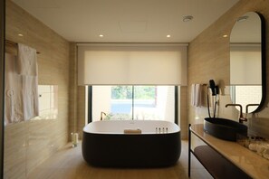 Een moderne badkamer met een vrijstaand bad, een grote spiegel en uitzicht op een wateroppervlak door een groot raam.