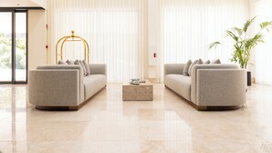 Uma sala de estar moderna com dois sofás, uma mesa de centro de mármore e uma janela ampla com cortinas leves.