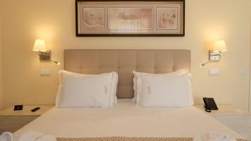A hotel room with a large bed, two bedside lamps, a framed picture above the bed, a bedside phone, and a remote control on the nightstand.