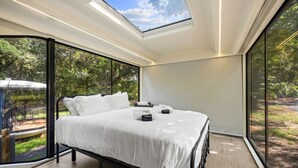 Une chambre à coucher moderne avec une lucarne, un lit recouvert de draps blancs et une vue sur l’extérieur.