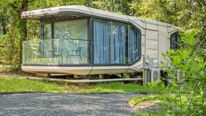 Une maison mobile moderne, de plain-pied, dotée d’un balcon en verre et située dans un endroit boisé.