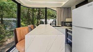 Une cuisine moderne dotée d’un plan de travail en marbre, d’un four encastré et d’un réfrigérateur. Une fenêtre offre une vue sur la verdure environnante.
