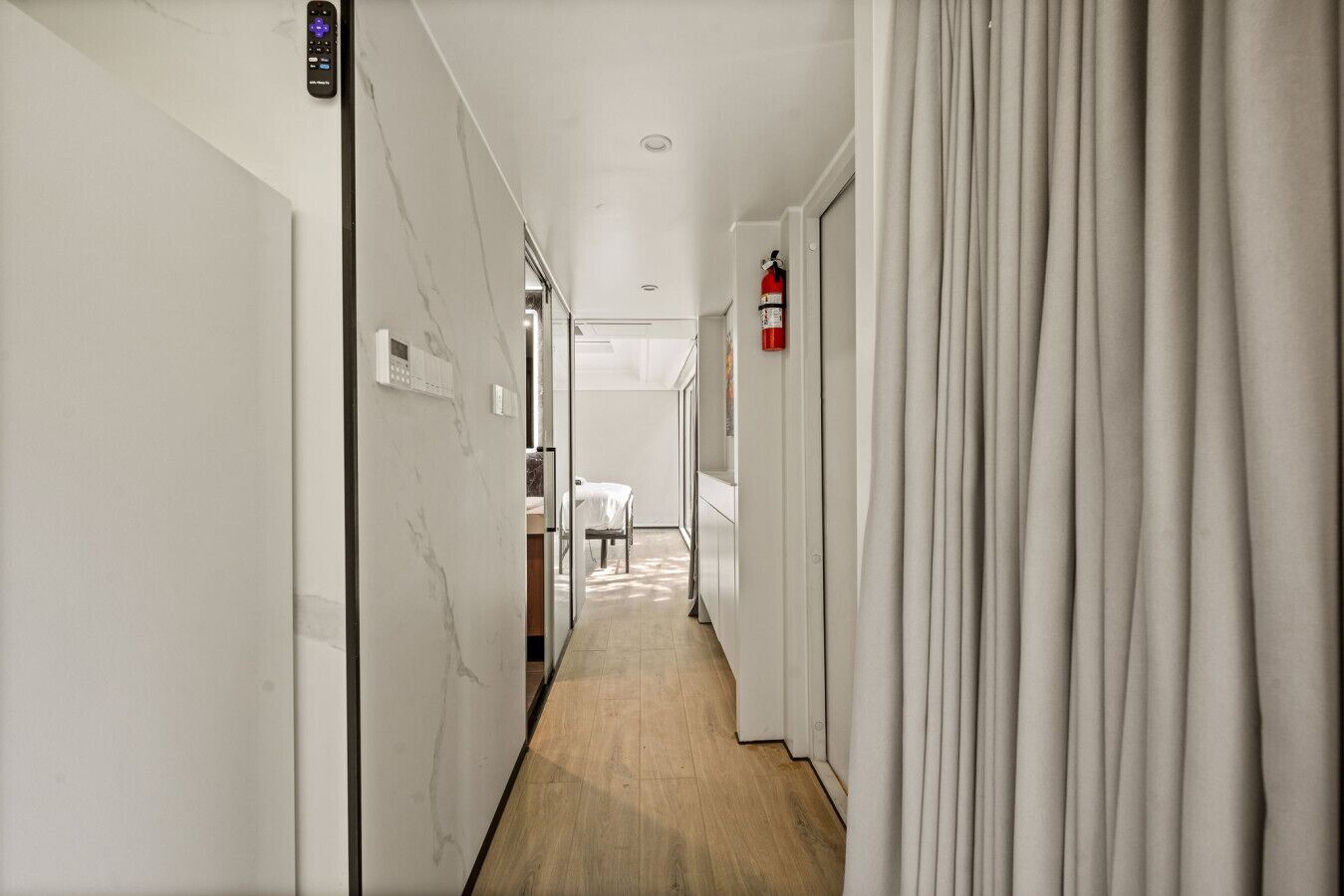 A hotel hallway with a marble wall, a fire extinguisher, and a bed in the distance.