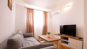 A modern living room with a grey sofa, a wooden coffee table, a flat-screen TV, and a small plant.
