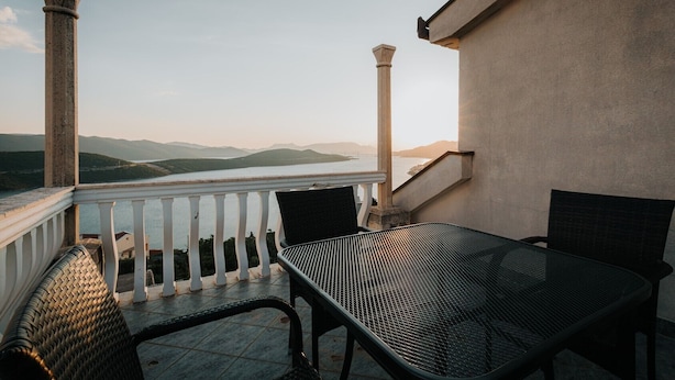A balcony with a table and chairs, overlooking a body of water and distant mountains.