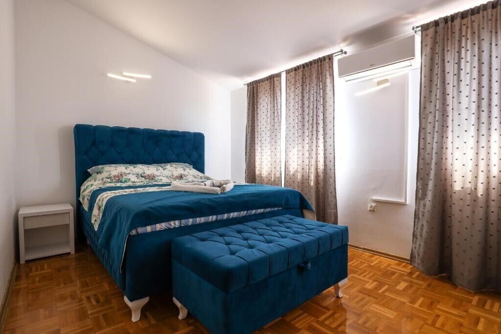Ein Schlafzimmer mit einem großen Bett, einer passenden Bank, einem Nachttisch und einem Fenster mit Vorhängen.