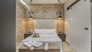 Ein Schlafzimmer mit Backsteinwand, einem großen Bett mit Kopfteil, Nachttischen und Pendelleuchten.