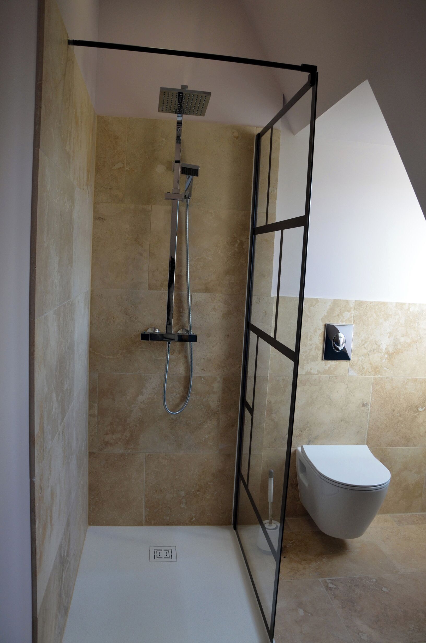 A shower area with a glass partition, a toilet, and beige tiled walls.