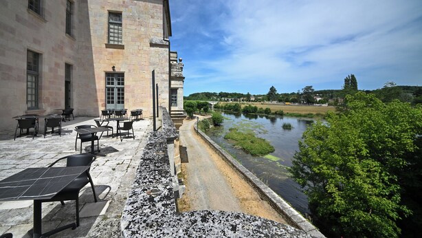 Een binnentuin met terras, een stenen gebouw en uitzicht op een rivier.