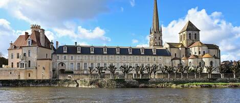 A historic building with a prominent tower and a church spire, situated by a river.