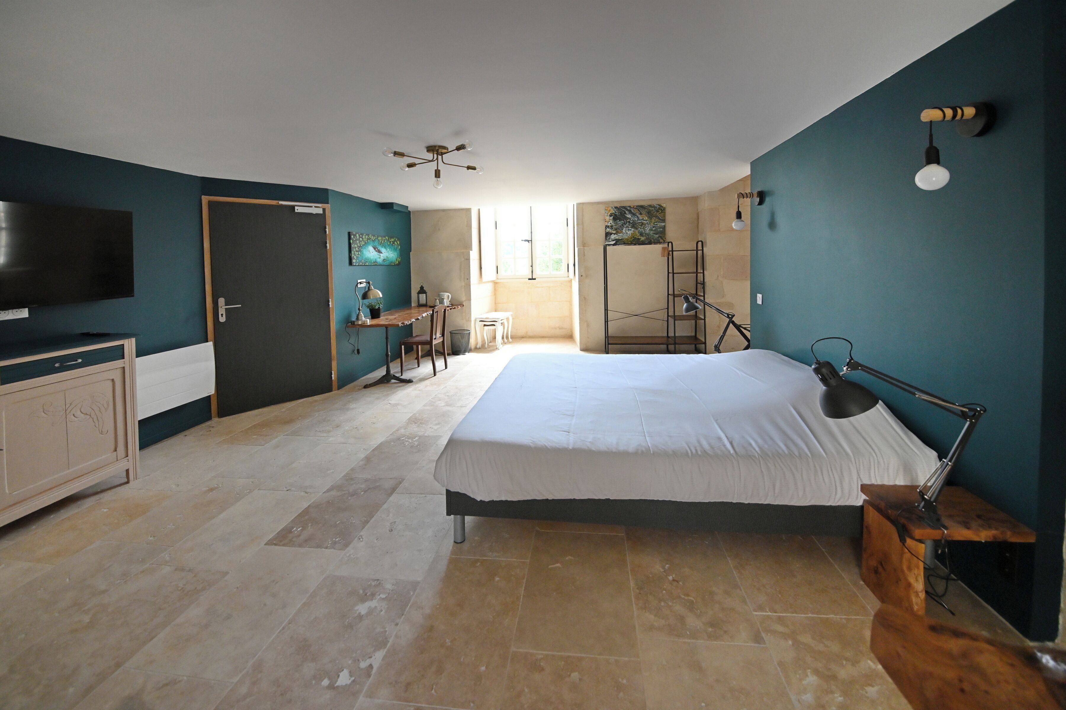 A bedroom with a large bed, a desk, a chair, a TV, and a ceiling fan.