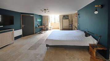 Una camera da letto con un letto grande, una scrivania, una sedia, una TV e una ventola a soffitto.